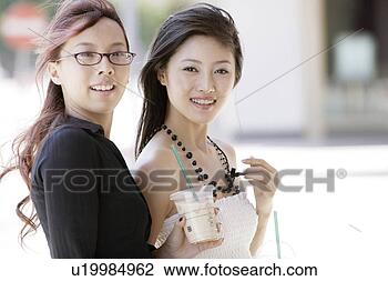 Stock Photo - two young women 
standing, holding 
two cups of beverage. 
fotosearch - search 
stock photos, 
pictures, images, 
and photo clipart