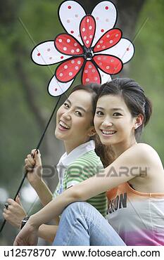 Picture - young women holding 
a flower-shaped 
windmill, grinning. 
fotosearch - search 
stock photos, 
pictures, images, 
and photo clipart