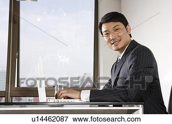 Picture - office man using 
laptop, sitting 
on chair, looking 
at camera. fotosearch 
- search stock 
photos, pictures, 
images, and photo 
clipart