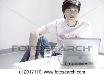 Stock Photography - young man sitting 
behind laptop 
and a glass of 
water. fotosearch 
- search stock 
photos, pictures, 
images, and photo 
clipart