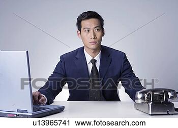 Stock Photography - young man sitting 
behind laptop 
and phone. fotosearch 
- search stock 
photos, pictures, 
images, and photo 
clipart