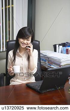 Stock Image - young woman calling 
and drinking in 
office. fotosearch 
- search stock 
photos, pictures, 
images, and photo 
clipart