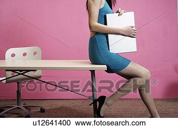 Stock Photography - young woman leaning 
on a desk, holding 
a laptop. fotosearch 
- search stock 
photos, pictures, 
images, and photo 
clipart