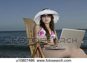 Stock Photo - young woman playing 
laptop on wooden 
chair on beach. 
fotosearch - search 
stock photos, 
pictures, images, 
and photo clipart