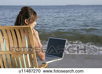Stock Photography - young woman sitting 
on wooden chair, 
looking at laptop 
on beach. fotosearch 
- search stock 
photos, pictures, 
images, and photo 
clipart