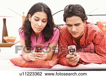 Stock Photo - young couple lying 
on the bed and 
holding mobile 
phones. fotosearch 
- search stock 
photos, pictures, 
images, and photo 
clipart