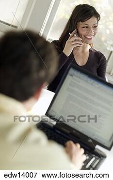 Picture - young man using 
laptop as wife 
talks on cell 
phone. fotosearch 
- search stock 
photos, pictures, 
images, and photo 
clipart
