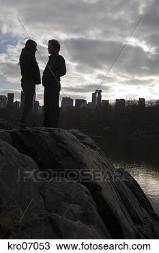 Stock Photo - low angle view 
of couple standing 
on rock with view 
of city skyline. 
fotosearch - search 
stock photos, 
pictures, images, 
and photo clipart