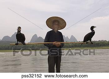 Stock Photo - senior asian man 
wearing conical 
hat with two birds 
on pole,  li. 
fotosearch - search 
stock photos, 
pictures, images, 
and photo clipart