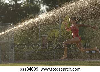 Stock Photograph - woman in swimwear 
running through 
sprinkler. fotosearch 
- search stock 
photos, pictures, 
images, and photo 
clipart