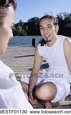 Arquivo de Fotografias - dois,  jovem, 
 men,  sentando, 
 jetty,  sorrindo, 
 close-up. fotosearch 
- busca de fotos, 
imagens e clipart