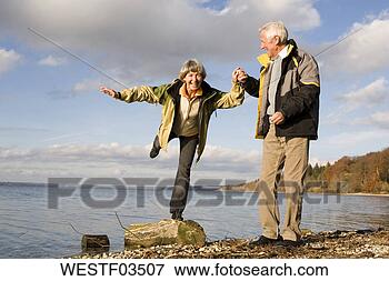Picture - senior couple 
hand in hand, 
woman standing 
on tree trunk. 
fotosearch - search 
stock photos, 
pictures, images, 
and photo clipart