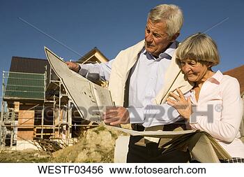 Stock Photo - senior couple 
holding plan in 
front of partially 
built house. fotosearch 
- search stock 
photos, pictures, 
images, and photo 
clipart