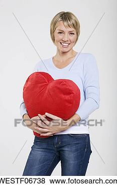 Banco de Imagem - jovem,   mulher, 
  segurando,  
 heart-shaped, 
  almofada,   
sorrindo. fotosearch 
- busca de fotos, 
imagens e clipart