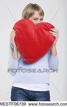 Arquivo Fotográficos - jovem,   mulher, 
  segurando,  
 heart-shaped, 
  almofada,   
sorrindo. fotosearch 
- busca de fotos, 
imagens e clipart