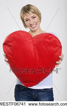 Arquivo de Fotografia - jovem,   mulher, 
  segurando,  
 heart-shaped, 
  almofada,   
sorrindo. fotosearch 
- busca de fotos, 
imagens e clipart