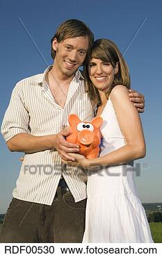 Stock Photography - germany, bavaria, 
young couple holding 
piggy bank, smiling, 
portrait. fotosearch 
- search stock 
photos, pictures, 
images, and photo 
clipart